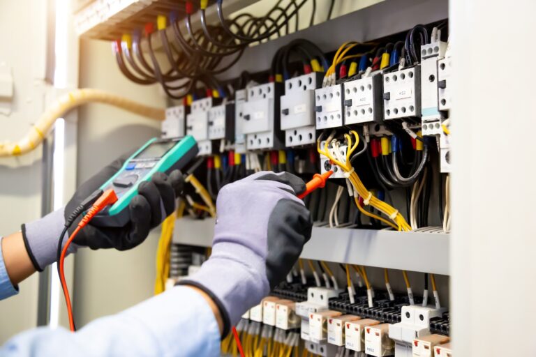 Electrical engineer using digital multi-meter measuring equipment to checking electric current voltage at circuit breaker and cable wiring system in main power distribution board